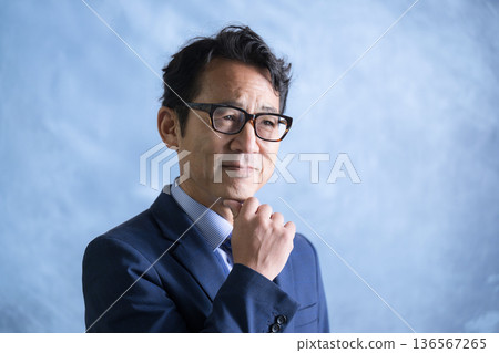A businessman in a suit and glasses thinking with his hand on his chin A businessman in a suit and glasses thinking with his hand on his chin 136567265