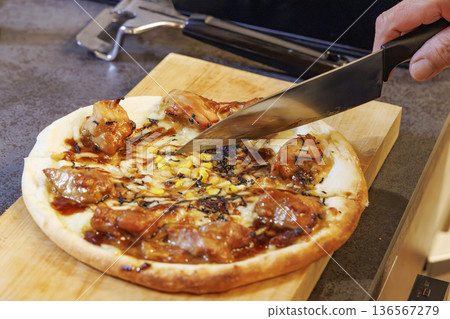 Teriyaki chicken pizza cut into pieces with a knife 136567279