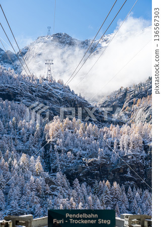 Ropeway from Furi to Trockener Steck with misty snow-capped mountains in the background. Zermatt, Vallee 136567303