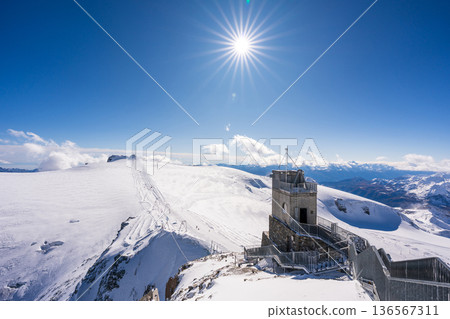 Stone elevator tower and metal stairs at the Klein Matterhorn observation deck, with sunlight. Zermatt, Vulcano 136567311