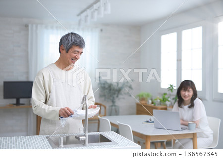 一位女士正在和一位六十多歲、正在廚房洗碗的男士說話。 136567345