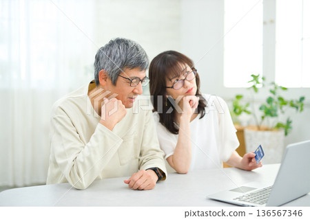 一對六十多歲的夫婦在客廳看著電腦和撲克牌。 136567346