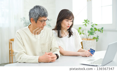 A couple in their 60s looking at a computer and cards in the living room A couple in their 60s looking at a computer and cards in the living room 136567347