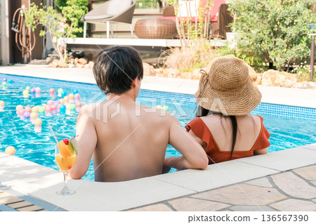 A couple in swimsuits playing by the pool at a resort hotel on a trip, back view of a married couple A couple in swimsuits playing by the pool at a resort hotel on a trip, back view of a married couple 136567390
