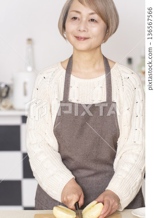 Senior woman peeling an apple in the kitchen 136567566