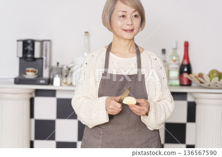 Senior woman peeling an apple in the kitchen 136567590