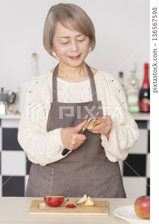 Senior woman peeling an apple in the kitchen 136567598