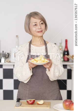 Senior woman peeling an apple in the kitchen 136567617