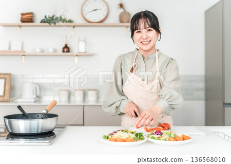 年輕的亞裔女子穿著圍裙在廚房做飯 年輕的亞裔女子穿著圍裙在廚房做飯 136568010