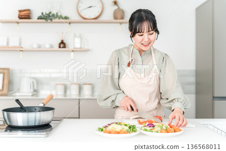 年輕的亞裔女子穿著圍裙在廚房做飯 年輕的亞裔女子穿著圍裙在廚房做飯 136568011