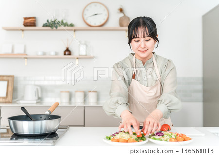 Young Asian woman in an apron cooking in the kitchen Young Asian woman in an apron cooking in the kitchen 136568013