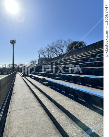 Sunlight pouring into the spectator seats at a sports field with night lights Sunlight pouring into the spectator seats at a sports field with night lights 136568447