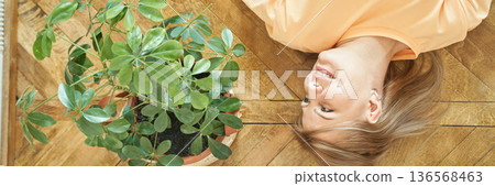 Caucasian mature female relaxing indoors with green houseplant on wooden floor Caucasian mature female relaxing indoors with green houseplant on wooden floor 136568463