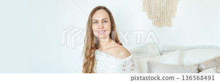 Young caucasian female in white top smiling in minimalist room with textured Young caucasian female in white top smiling in minimalist room with textured 136568491