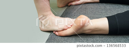 Foot massage therapy session with close-up of bare feet on carpeted floor 136568533