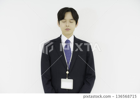 Portrait of a young Japanese man in a suit with his eyes closed on a white background Portrait of a young Japanese man in a suit with his eyes closed on a white background 136568715