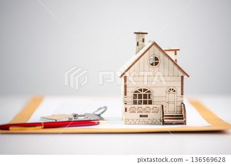 Miniature wooden house on document envelope with pen and house keys on white background, representing real estate paperwork, mortgage approval, home buying process and financial security. mortgage 136569628
