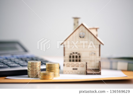 Miniature wooden house beside stacks of coins on paperwork with calculator in background, showing mortgage budgeting, real estate investment planning, long-term financial security. investment planning Miniature wooden house beside stacks of coins on paperwork with calculator in background, showing mortgage budgeting, real estate investment planning, long-term financial security. investment planning 136569629