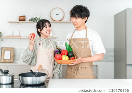 一對年輕的亞裔男女在廚房裡拿著蔬菜，他們是夫妻。 136570366