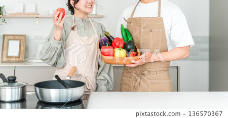 一對年輕的亞裔男女在廚房裡拿著蔬菜，他們是夫妻。 136570367