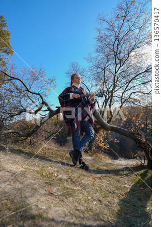 Blonde woman playing guitar ukulele outdoors in autumn forest. Concept of sound therapy, mental health and wellness rituals. Calmness tranquility audio-sensory practices. Aura farming Blonde woman playing guitar ukulele outdoors in autumn forest. Concept of sound therapy, mental health and wellness rituals. Calmness tranquility audio-sensory practices. Aura farming 136570417