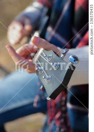Close up of female hands play ukulele in autumnal park. Young woman plays guitar musical instrument outside in nature fall time. Audio music healing 136570435