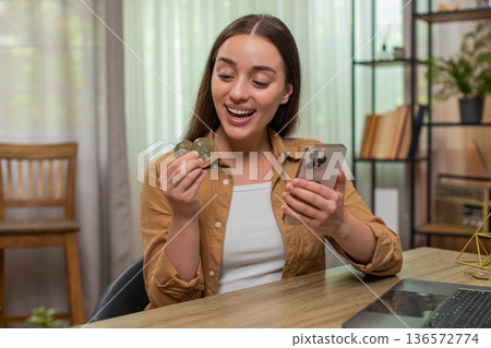 Young woman smiles at smartphone after closing bitcoin trade watching crypto price line with joy now 136572774
