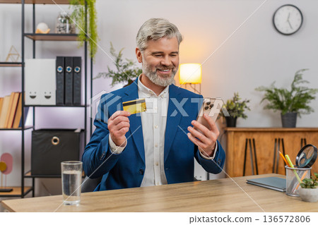 Middle-aged businessman confirms payment on smartphone holding credit card smiling at smooth service Middle-aged businessman confirms payment on smartphone holding credit card smiling at smooth service 136572806