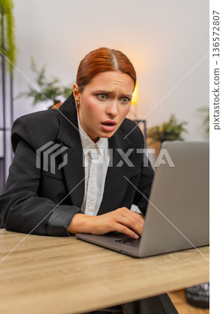 Young businesswoman checks bills on laptop spots error eyes widen and fixes numbers swiftly relieved Young businesswoman checks bills on laptop spots error eyes widen and fixes numbers swiftly relieved 136572807