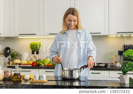 Young woman slowly seasoning homemade soup in pot on electric cooktop for healthy lunch at home 136572832