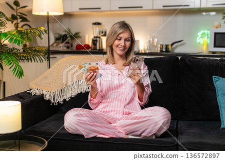 Woman counts money cash euros with smartphone plans budget notes check salary income saving record Woman counts money cash euros with smartphone plans budget notes check salary income saving record 136572897