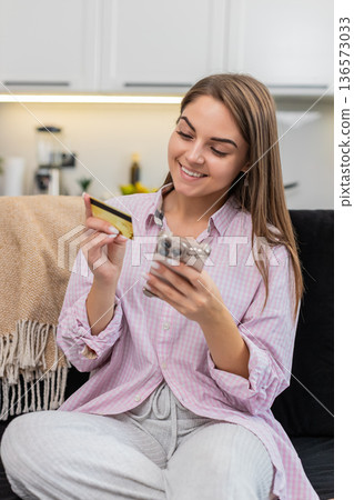 Young woman pays online order with smartphone and credit card taps pay smiles after secure purchase 136573033