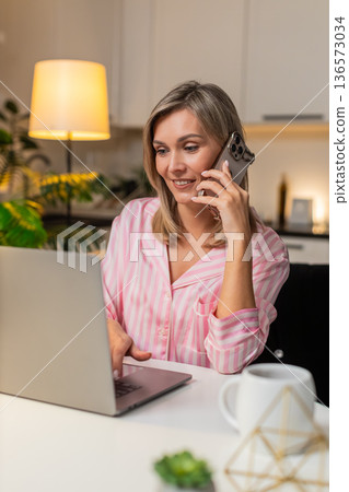 Adult woman works on laptop talks on smartphone multitask productive remote clear voice focus call 136573034
