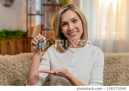 Adult woman celebrating new apartment at home, showing house keys proudly to camera with smile Adult woman celebrating new apartment at home, showing house keys proudly to camera with smile 136573048