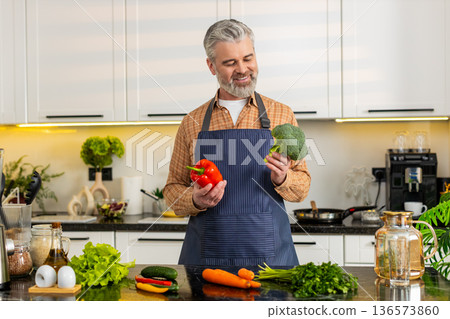 Middle-aged man smiling holding fresh pepper with broccoli for healthy diet prep at home kitchen fit Middle-aged man smiling holding fresh pepper with broccoli for healthy diet prep at home kitchen fit 136573860