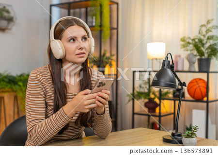 Young woman in headphones listens to productivity podcast and writes ideas on smartphone for tasks 136573891