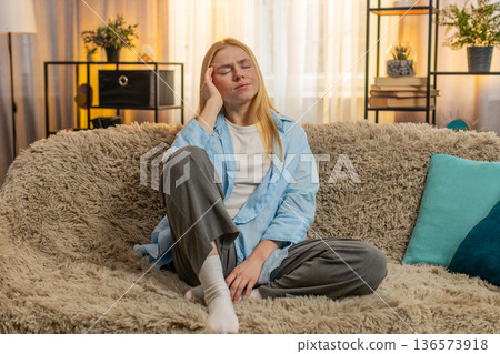 Young woman massaging head at home, migraine tension, closed eyes, sofa fatigue, stressful moment 136573918