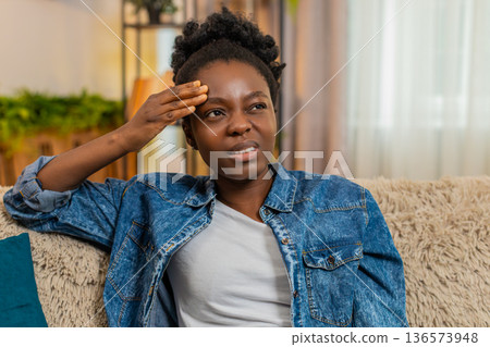 African American woman massaging head on sofa with frustration from headache after studying hard African American woman massaging head on sofa with frustration from headache after studying hard 136573948