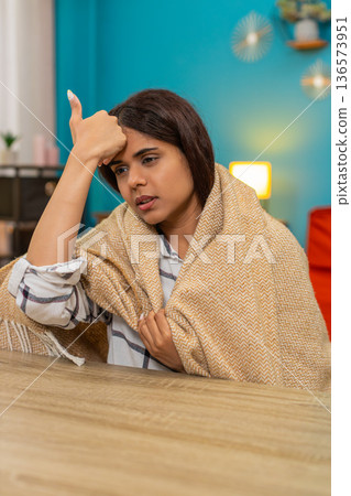 Indian woman wrapped in blanket touches forehead checking temperature feeling worried fever indoors 136573951