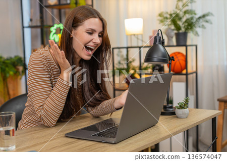 Young woman reads high project score on laptop shouts wow smiles wide and adds thank you review note 136574047