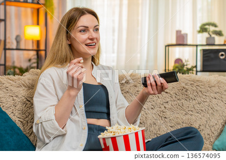 Adult woman laughing while watching comedy on television at home, joyful expression and relaxed mood Adult woman laughing while watching comedy on television at home, joyful expression and relaxed mood 136574095
