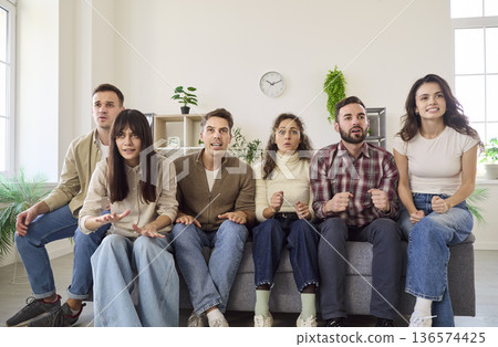 Friends watching tense football match on TV at home, anxious fans on sofa 136574425