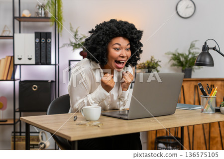 African American businesswoman excited celebrates laptop victory project approval and big game win African American businesswoman excited celebrates laptop victory project approval and big game win 136575105