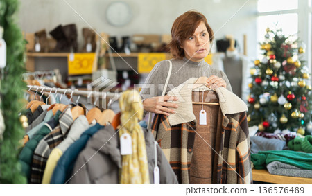 Woman chooses jacket and coat for the winter period in fashionable clothing store 136576489