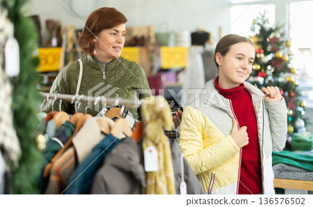 Woman chooses jacket and coat for the winter period in fashionable clothing store Woman chooses jacket and coat for the winter period in fashionable clothing store 136576502