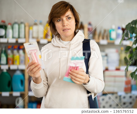 Woman carefully selects razor for shaving in the household goods department of supermarket 136576552