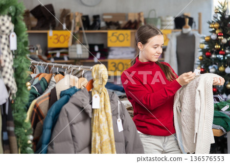 Teen girl picks up clothes and chooses sweater, New Year Eve sale Teen girl picks up clothes and chooses sweater, New Year Eve sale 136576553
