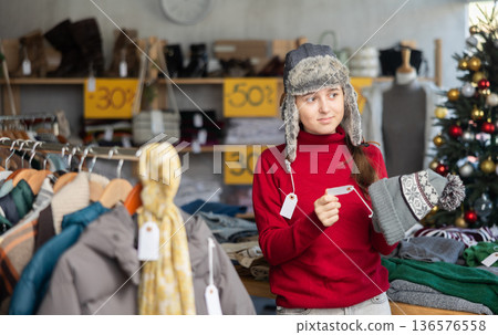 Teen girl try on winter fur hat in front of mirror in clothes store Teen girl try on winter fur hat in front of mirror in clothes store 136576558