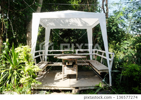 White cloth summer pavilion with rustic wooden outdoor dining table in natural sunlight decorated in garden White cloth summer pavilion with rustic wooden outdoor dining table in natural sunlight decorated in garden 136577274