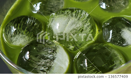 Vibrant green matcha latte being poured into a glass with ice cubes creating a refreshing 136577409